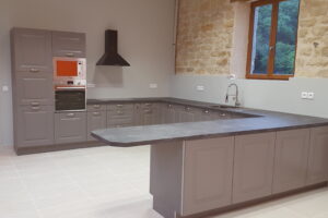 Cuisine grise sur mesure avec îlot central, plan de travail foncé et mur en pierre apparente dans une rénovation de maison ancienne.