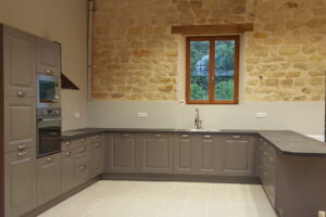 Cuisine grise sur mesure avec mur en pierre apparente, agencement en U et plan de travail foncé après rénovation complète